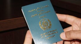 The photo features an Afghan passport held in the hands of an individual.