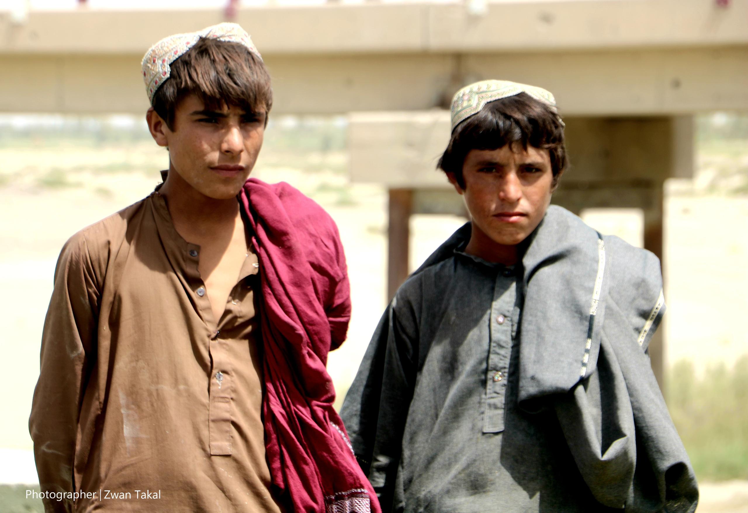 The image shows two Afghan teenagers, their faces reflecting youthful freshness, yet their clothes and eyes reveal their poverty.
