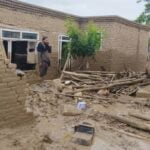 An Afghan man stands in the doorway of his mud-brick home, which has been partly destroyed by mud and debris from recent floods, talking on the phone in Baghlan.