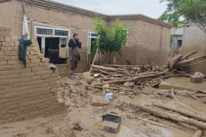 An Afghan man stands in the doorway of his mud-brick home, which has been partly destroyed by mud and debris from recent floods, talking on the phone in Baghlan.