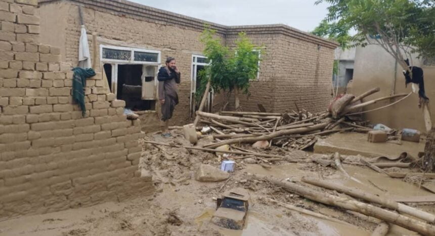 An Afghan man stands in the doorway of his mud-brick home, which has been partly destroyed by mud and debris from recent floods, talking on the phone in Baghlan.