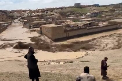 Floodwaters inundate a village in Ghor, Afghanistan, causing severe damage to homes and infrastructure. Residents observe the destruction from a distance.
