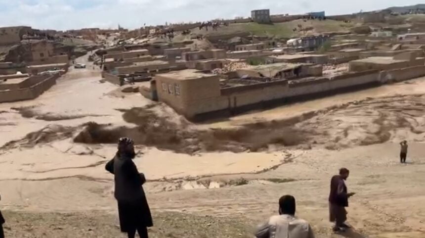 Floodwaters inundate a village in Ghor, Afghanistan, causing severe damage to homes and infrastructure. Residents observe the destruction from a distance.