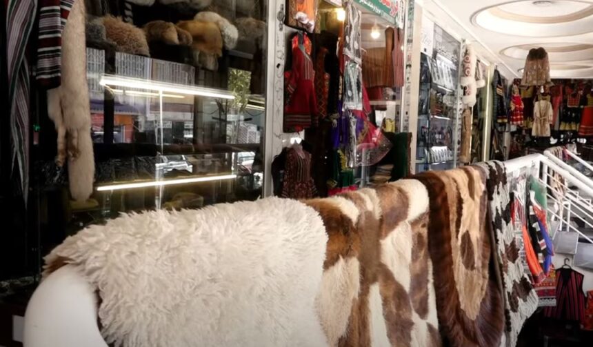 A shop displaying a variety of traditional Afghan coats and garments. The storefront features vibrant and intricately designed Afghan clothing, including coats with fur and embroidery. The shop is filled with an array of traditional textiles and crafts, showcasing the rich cultural heritage and craftsmanship of Afghanistan.