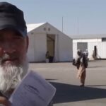 An elderly Afghan worker at the Islam Qala border between Iran and Afghanistan holds up a work permit he received in Iran. He explains to reporters that Iranian authorities forcibly deported him, leaving his wages for several months unpaid by his employer.